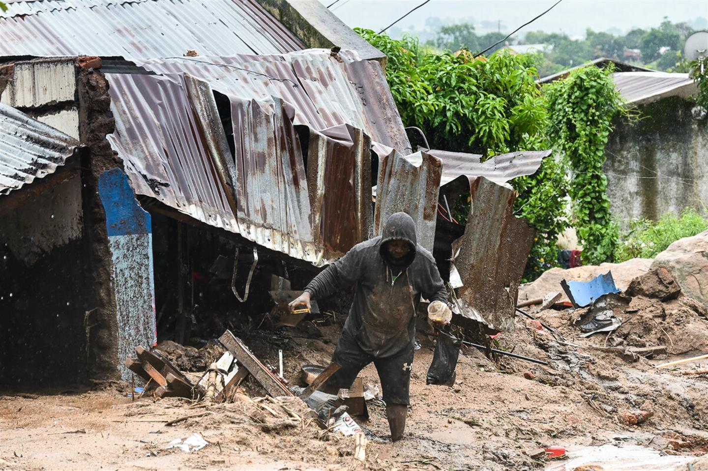 Een man raapt iets op voor zijn huis dat verwoest is door modderlawines en zware regen