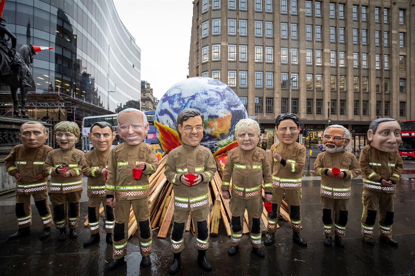  Oxfam-activisten in Glasgow, verkleed als o.m. premier Rutte en andere regeringsleiders, die als ineffectieve brandweermannen er niet in slagen een brandende aarde te blussen, op de laatste dag van de VN-klimaattop