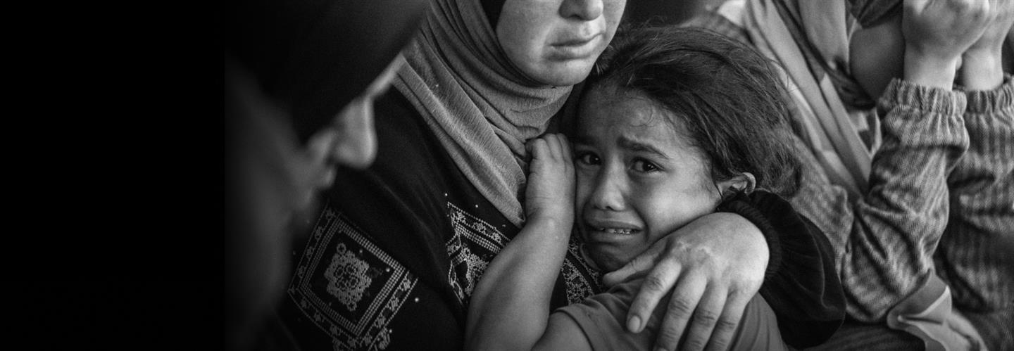 Een kind kijkt angstig en verdrietig in de camera, in de armen van een vrouw