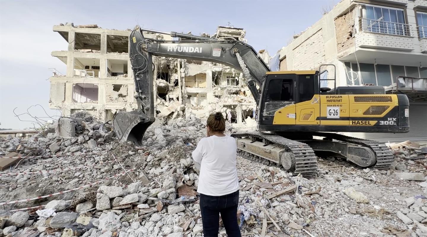 Iemand kijkt naar het puin en een graafmachine in het aardbevingsgebied in Turkijke