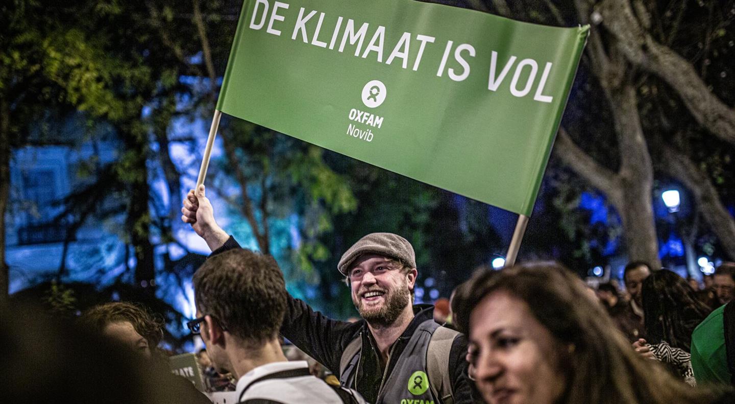 Een man staat met een spandoek in zijn hand met daarop 'De klimaat is vol'