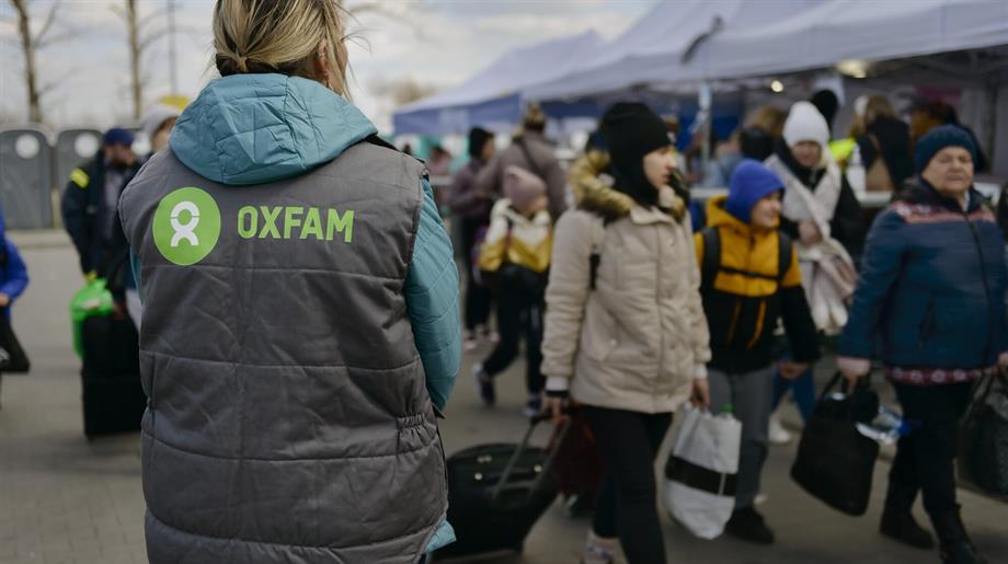 Vluchtelingen aan de grens, onderweg met hun spullen, samen met een Oxfam-medewerker vanaf de rug gezien.